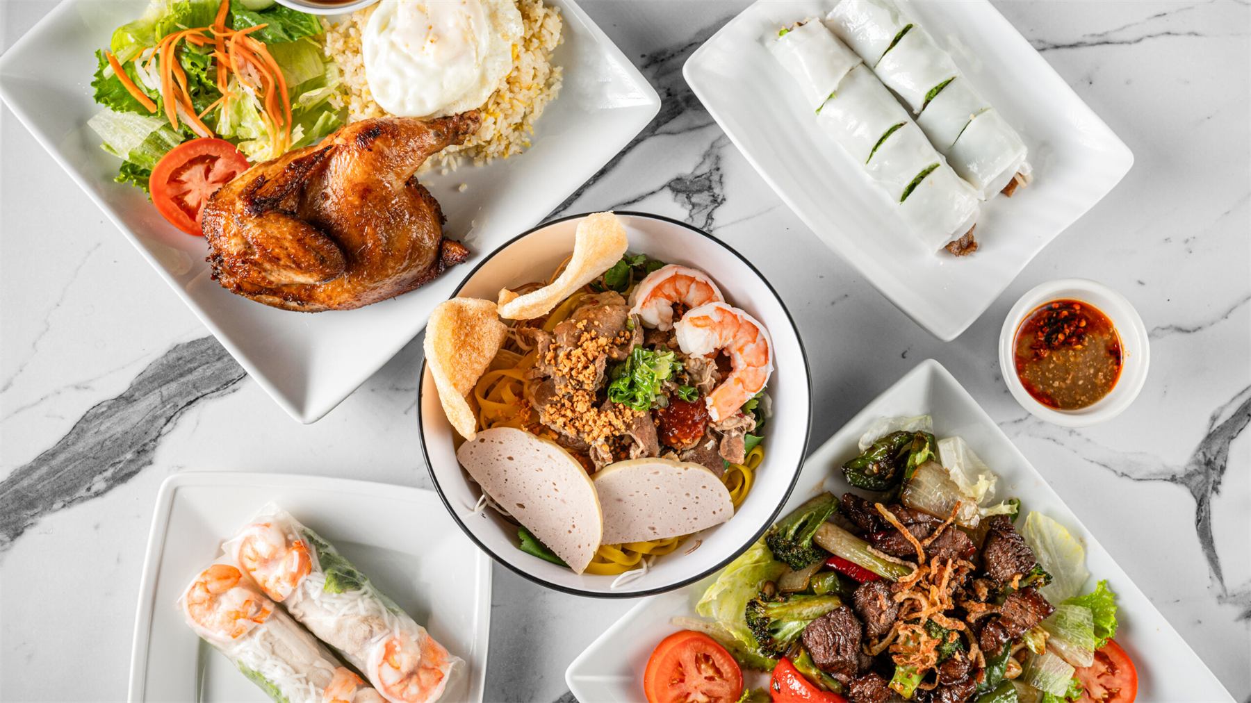 Waterfall fried chicken, Mì Quảng, Bánh Cuốn, spring rolls and shaking beef on a marble table